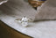 This custom engagement ring created by The North Way Studio is shown in reclaimed white gold with an oval diamond center resting on a marble table facing the viewer. This design features whittled gold leaves, two natural pear cut diamonds, and a scattering of diamond dewdrops.