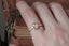 A rose cut diamond ring designed and crafted by The North Way Studio in collaboration with Claire Pettibone and cast in reclaimed gold is shown sitting upon a hand resting atop weathered books.