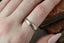 The Elder King Band by The North Way Studio is a hand-carved golden wedding band, shown here on a woman's finger, with her hand resting atop antique books. 