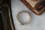 The Elder King Band by The North Way Studio is a hand-carved golden wedding band, shown here in an overhead view in front of antique books atop a white marble tabletop.