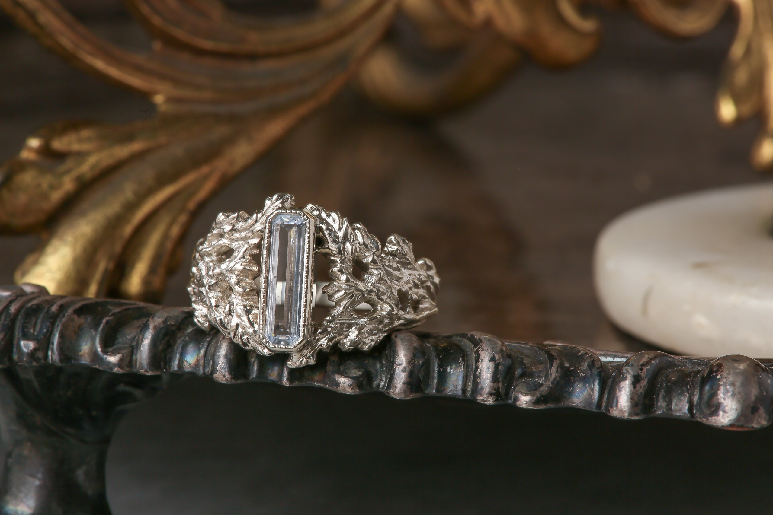 An elongated pale blue sapphire sits within a hand-carved band of white gold in this ring designed by The North Way Studio. The ready to ship engagement ring is shown facing the viewer.