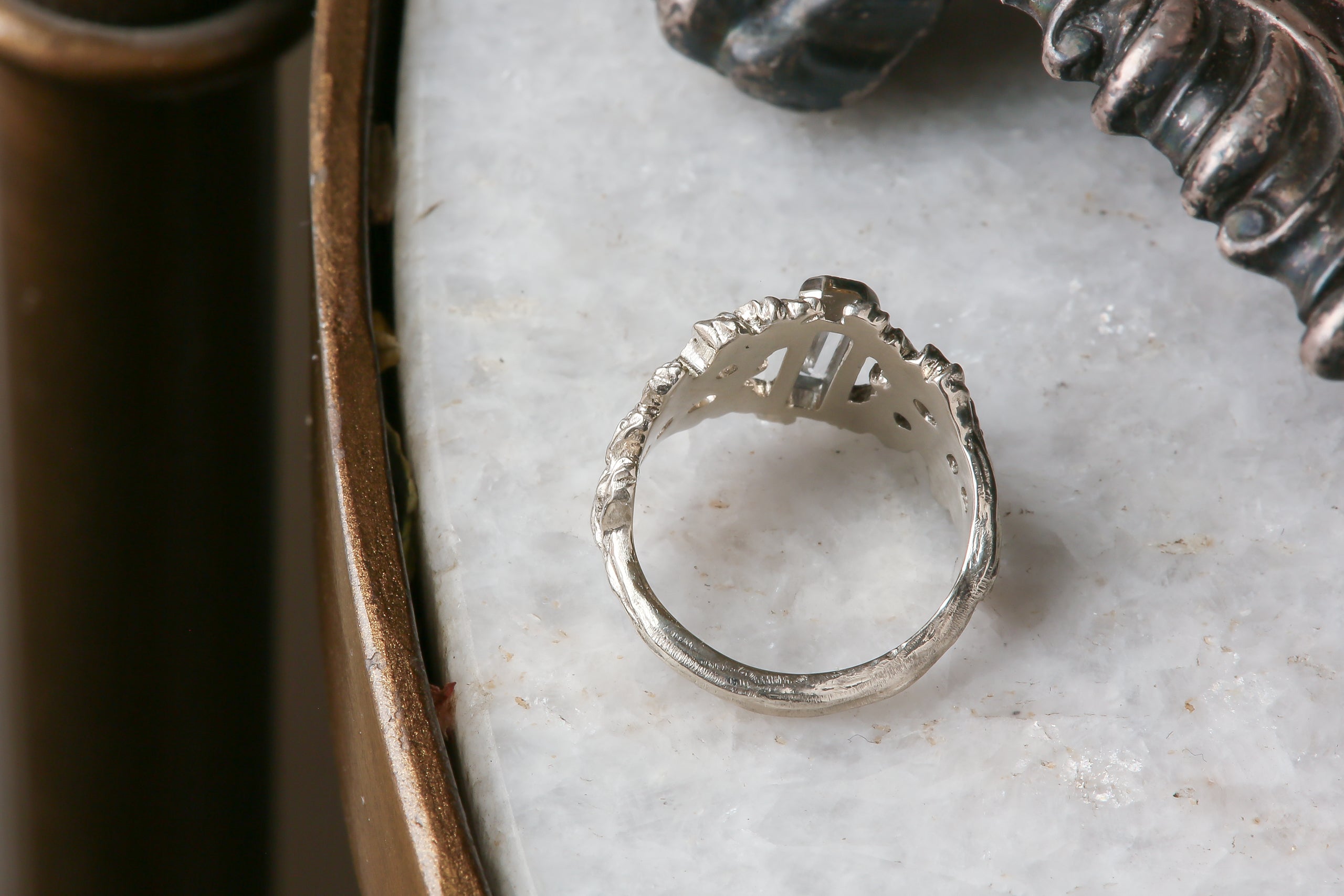 An elongated pale blue sapphire sits within a hand-carved band of white gold in this ring designed by The North Way Studio. The ready to ship engagement ring is shown facing away from the viewer.