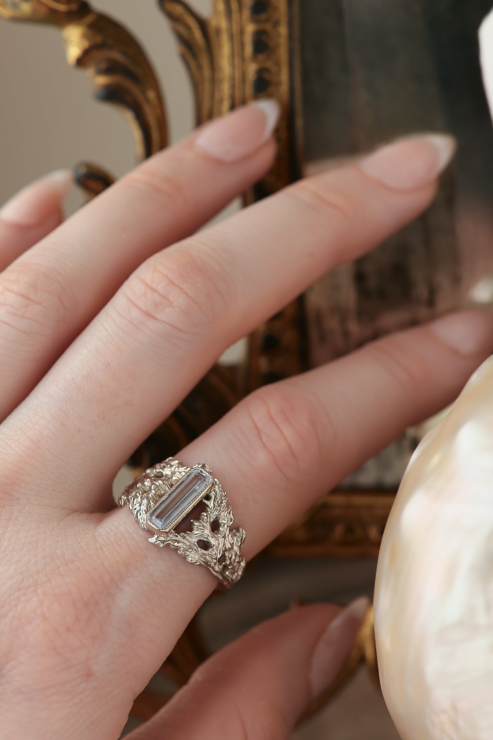 An elongated pale blue sapphire sits within a hand-carved band of white gold in this ring designed by The North Way Studio. The ready to ship engagement ring is shown on a woman's first finger.