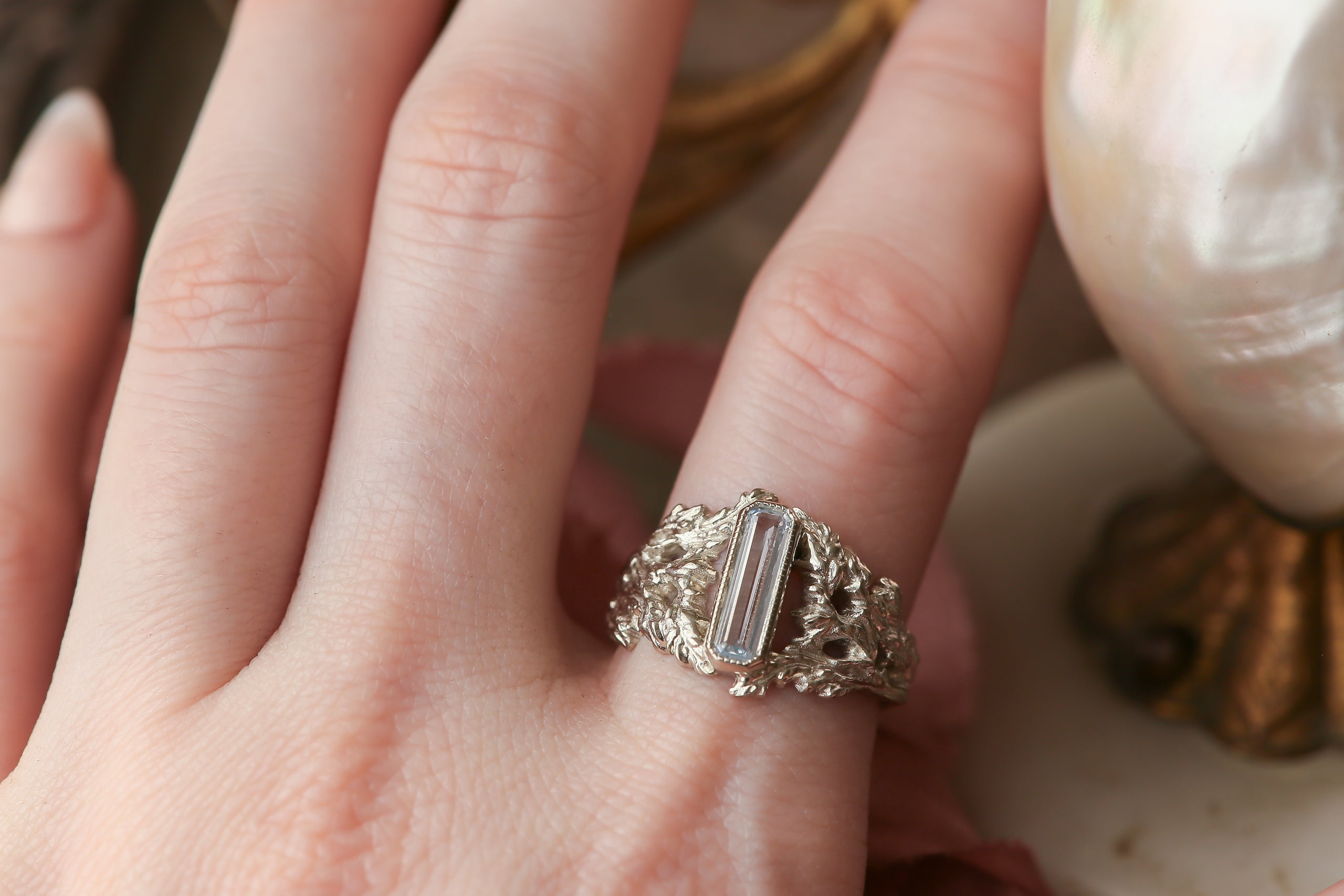 An elongated pale blue sapphire sits within a hand-carved band of white gold in this ring designed by The North Way Studio. The ready to ship engagement ring is shown on a woman's first finger.