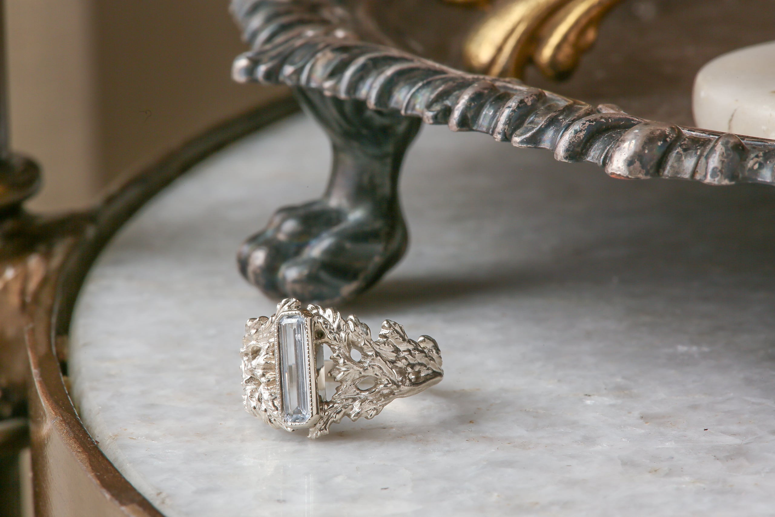 An elongated pale blue sapphire sits within a hand-carved band of white gold in this ring designed by The North Way Studio. The ready to ship engagement ring is shown facing the viewer slightly turned left.