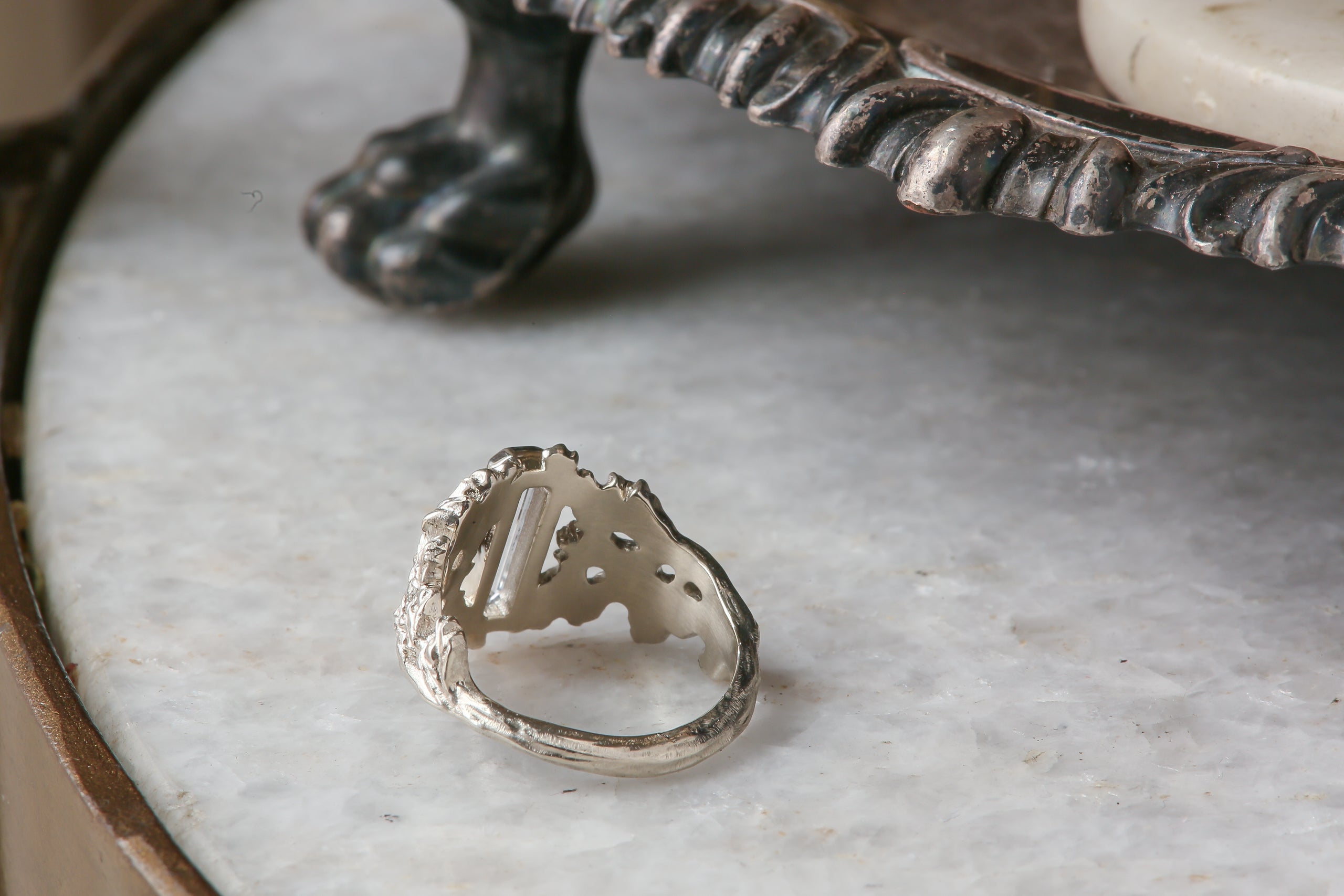 An elongated pale blue sapphire sits within a hand-carved band of white gold in this ring designed by The North Way Studio. The ready to ship engagement ring is shown facing away from the viewer.