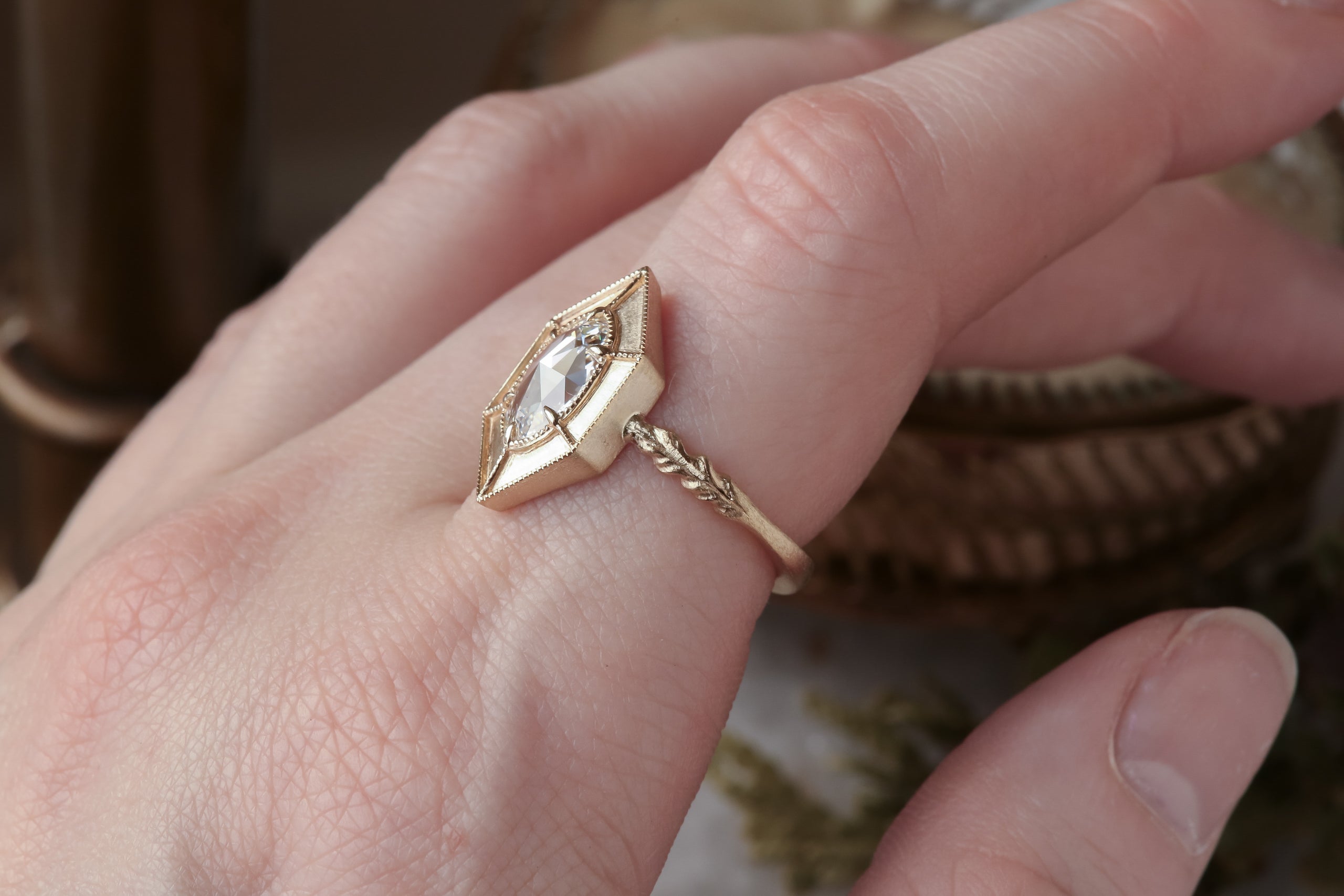 A relic of whittled gold and hues of an awakening gilded dawn. Carved 14 karat yellow gold cocoons about an elongated oval rose cut lab grown diamond. The Helm Ring in lab grown oval rose cut diamond is a ready to ship ring designed and sold at The North Way Studio. This diamond ring is shown worn on the first finger of a woman's hand.