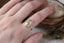 A relic of whittled gold and hues of an awakening gilded dawn. Carved 14 karat yellow gold cocoons about an elongated oval rose cut lab grown diamond. The Helm Ring in lab grown oval rose cut diamond is a ready to ship ring designed and sold at The North Way Studio. This diamond ring is shown worn on the first finger of a woman's hand.