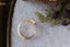 A relic of whittled gold and hues of an awakening gilded dawn. Carved 14 karat yellow gold cocoons about an elongated oval rose cut lab grown diamond. The Helm Ring in lab grown oval rose cut diamond is a ready to ship ring designed and sold at The North Way Studio. This diamond ring is shown resting on a marble shelf and viewed from above.