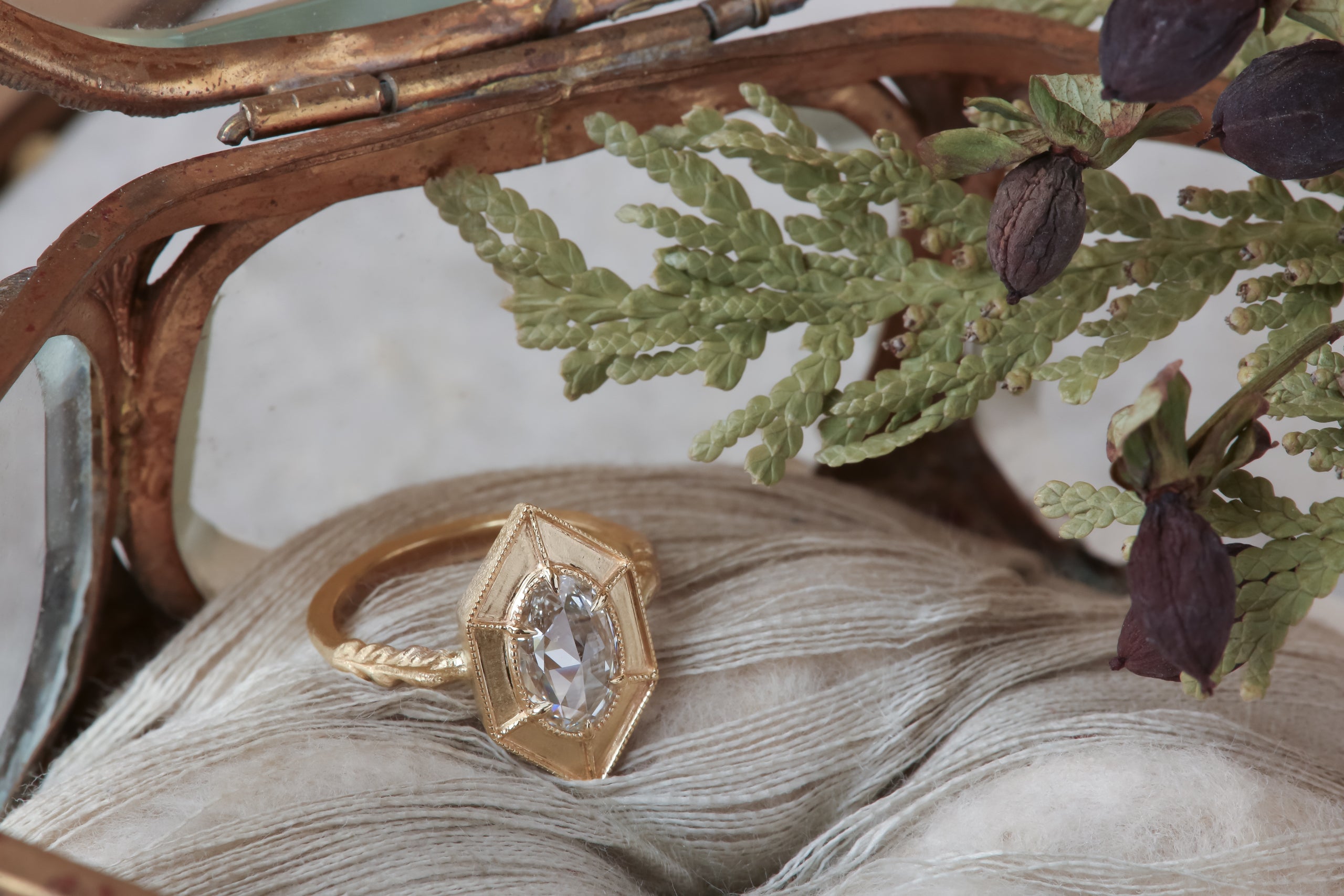 A relic of whittled gold and hues of an awakening gilded dawn. Carved 14 karat yellow gold cocoons about an elongated oval rose cut lab grown diamond. The Helm Ring in lab grown oval rose cut diamond is a ready to ship ring designed and sold at The North Way Studio. This fantasy engagement ring is shown resting in an antique jewelry box.