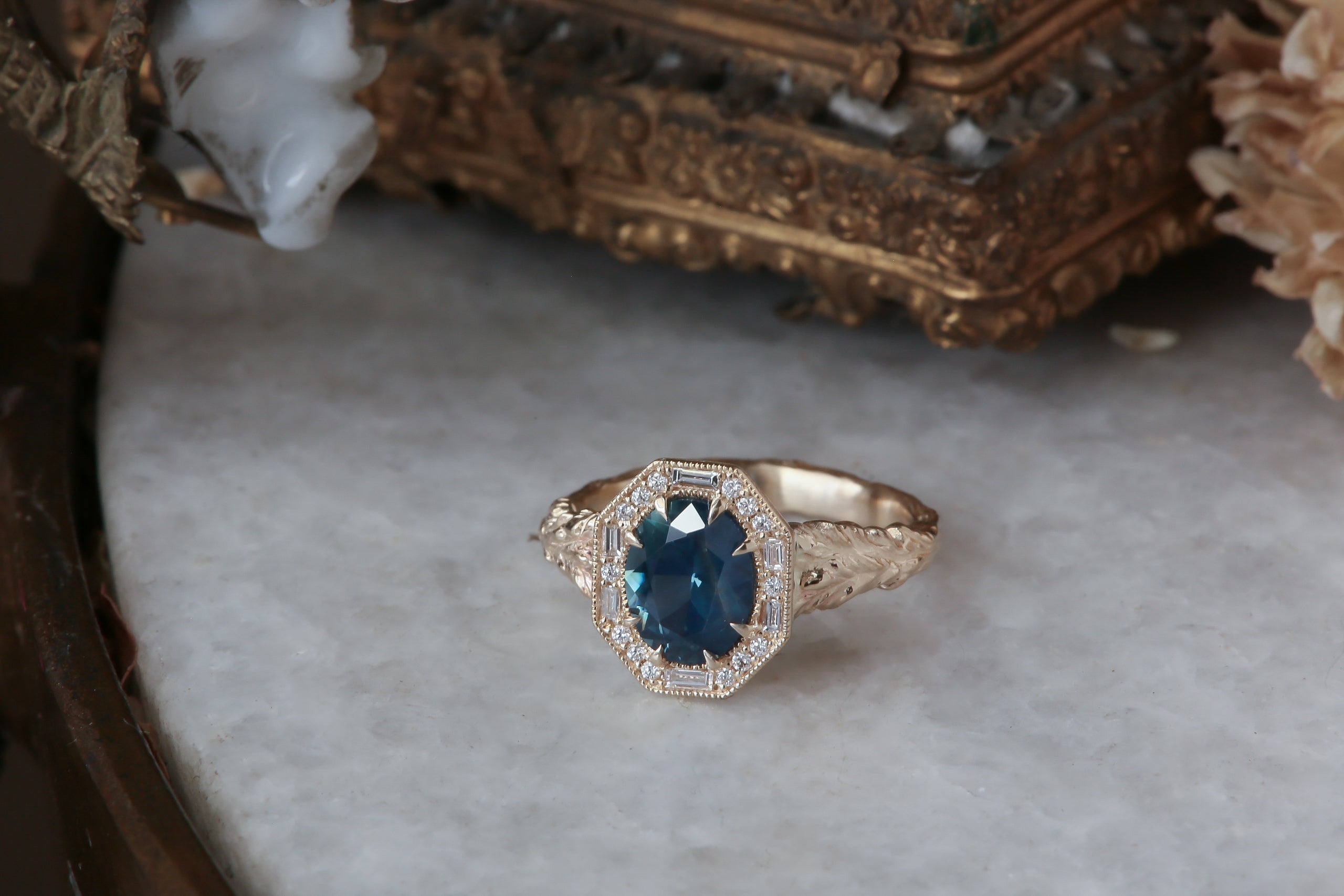 A large blue sapphire sits in the middle of this ready to ship engagement ring designed by The North Way Studio shown facing the viewer. A halo of diamonds surrounds the center stone. The band is hand-carved reclaimed gold.