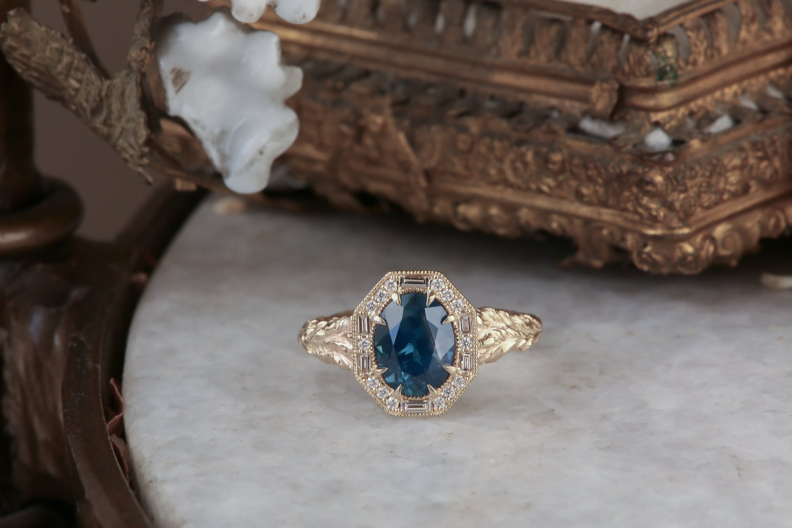 A large blue sapphire sits in the middle of this ready to ship engagement ring designed by The North Way Studio shown facing the viewer. A halo of diamonds surrounds the center stone. The band is hand-carved reclaimed gold.