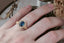 A large blue sapphire sits in the middle of this ready to ship engagement ring designed by The North Way Studio shown on someone's ring finger. A halo of diamonds surrounds the center stone. The band is hand-carved reclaimed gold.