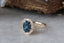 A large blue sapphire sits in the middle of this ready to ship engagement ring designed by The North Way Studio shown facing slightly left. A halo of diamonds surrounds the center stone. The band is hand-carved reclaimed gold.