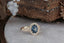 A large blue sapphire sits in the middle of this ready to ship engagement ring designed by The North Way Studio shown facing slightly right. A halo of diamonds surrounds the center stone. The band is hand-carved reclaimed gold.