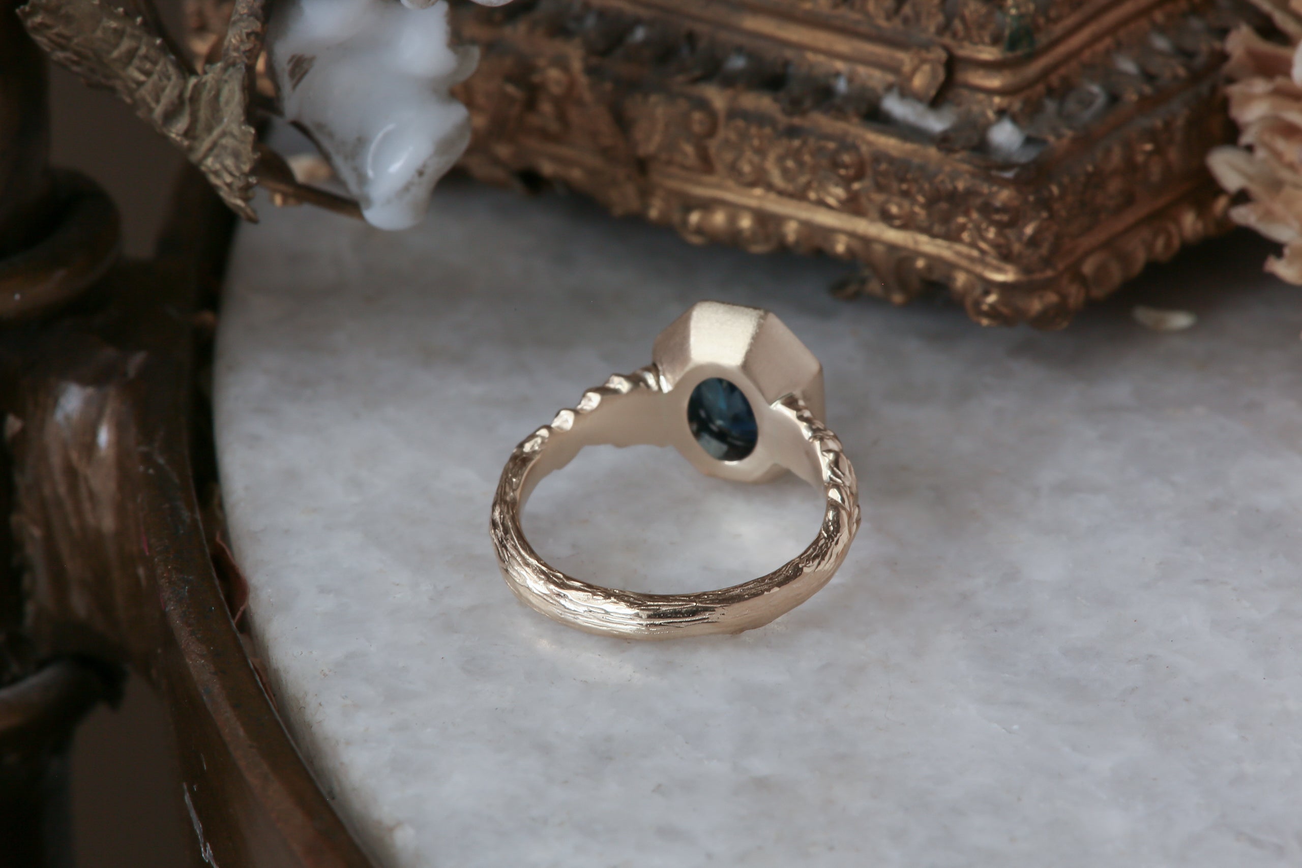 A large blue sapphire sits in the middle of this ready to ship engagement ring designed by The North Way Studio shown facing away from the viewer. A halo of diamonds surrounds the center stone. The band is hand-carved reclaimed gold.