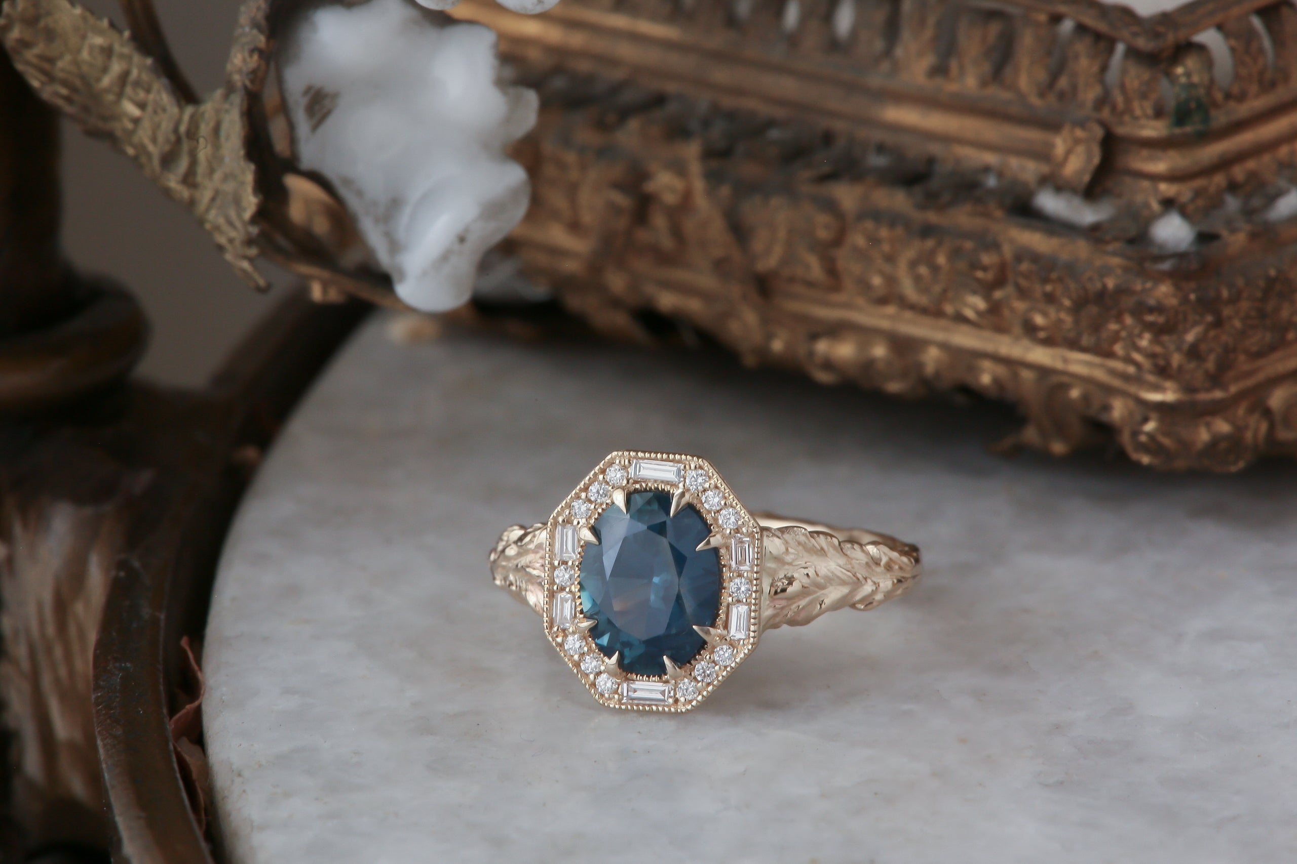 A large blue sapphire sits in the middle of this ready to ship engagement ring designed by The North Way Studio shown facing the viewer. A halo of diamonds surrounds the center stone. The band is hand-carved reclaimed gold.