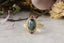 Petite sapphires of mismatched blush and berry tones are woven about a lush teal green sapphire, cocooned in rustic whittled gold in this ring designed by The North Way Studio in collaboration with Claire Pettibone.