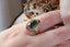 Petite sapphires of mismatched blush and berry tones are woven about a lush teal green sapphire, cocooned in rustic whittled gold in this ring designed by The North Way Studio in collaboration with Claire Pettibone and shown upon a hand.