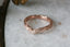 A wedding band of engraved gold freckled with three petite white diamonds is facing toward the left atop a white marble table. It is intricately engraved with geometric leaves with miligrain edges and was made by The North Way Studio.