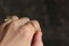 The side of a wedding band of engraved gold and freckled with three petite white diamonds is being shown on someone's finger. Intricately engraved geometric leaves with miligrain edges at The North Way Studio.