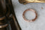 An overhead shot of a wedding band of engraved gold that is freckled with three petite white diamonds, atop a white marble table. It is intricately engraved with geometric leaves with miligrain edges and was made by The North Way Studio.