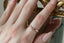 A wedding band of engraved gold is freckled with three petite white diamonds shown on someone's finger. Intricately engraved geometric leaves with miligrain edges at The North Way Studio.