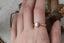 Lushly engraved gold cocoons around your choice of gemstone, while hidden diamonds are tucked below in this heirloom engagement ring setting crafted by The North Way Studio. This engraved ring is shown in 14 karat rose gold with an oval diamond center stone and worn on the index finger of a hand resting on an antique jewelry box.