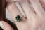 A large green sapphire oval and diamond engagement ring for elven queens and fae shown on the hand. 