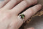 A large green sapphire oval and diamond engagement ring for elven queens and fae shown on the hand. 