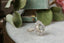 A diamond engagement ring designed and crafted by The North Way Studio in collaboration with Claire Pettibone and cast in reclaimed 18 karat white gold is shown sitting upon marble with a green fabric antique ring box and dried leaves in the background.