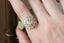 A diamond engagement ring designed and crafted by The North Way Studio in collaboration with Claire Pettibone and cast in reclaimed 18 karat white gold shown close up upon a hand.