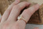 Reclaimed golden leaves are spun around your choice of center gemstone along with tiny diamond dew drops in this heirloom engagement ring setting designed and crafted by The North Way Studio. This ring is shown in 14 karat yellow gold with a large pear cut diamond center and worn on the index finger of a hand resting on an antique gold jewelry box. The hand is tilted to show the side profile of the ring.