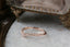 A ring made of a faintly curved rivulet of rose cut natural diamonds nestled against a hand-carved band of unfurling leaves and bark. Designed by The North Way Studio and shown here atop a white marble tabletop and facing left.