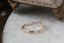 A ring made of a faintly curved rivulet of rose cut natural diamonds nestled against a hand-carved band of unfurling leaves and bark. Designed by The North Way Studio and shown here atop a white marble tabletop and facing away from the viewer. 