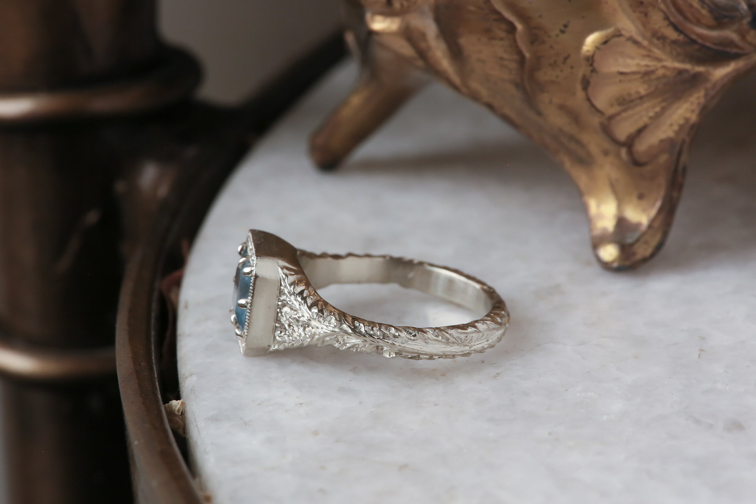 A square Montana sapphire sits within a halo of diamonds in this white gold, hand carved ring designed by The North Way Studio, shown facing far left.