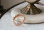 A golden wedding band designed by The North Way Studio. Hand-carved Scottish thistle and heather leaves shine in reclaimed gold. Shown leaning against a white plate on a white marble tabletop.