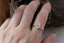 This heirloom engagement ring setting crafted by The North Way Studio features unfurling leaves and bark of carved gold, with petite claws to embrace a uniquely chosen center stone. This mythical ring is shown in 14 karat yellow gold with a pear cut diamond center. The engagement ring is shown on the index finger of a left hand.