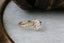 Petite claw prongs embrace a lab grown pear cut diamond in this ready to ship engagement ring designed by The North Way Studio. The band is gold and hand-carved with leaves and bark. Facing slightly right.