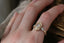 Three stone fantasy engagement ring featuring oval lab grown diamonds and medieval inspired engravings in reclaimed fine gold. A customizable engagement ring designed and crafted by The North Way Studio. This enchanting ring is shown in 14 karat yellow gold and is worn on a left hand.
