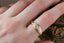 A customizable wide flower signet band with hand-carved lavender for protection. Shown in 10 karat yellow gold worn on a woman's finger.
