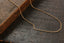 A delicate gold chain necklace draped over a dark wooden surface next to a rustic wooden block.