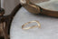 A gold wedding band with tiny diamonds faces right atop a white marble table at The North Way Studio.