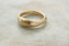 A textured, organic-shaped gold ring resting on a light beige stone surface.