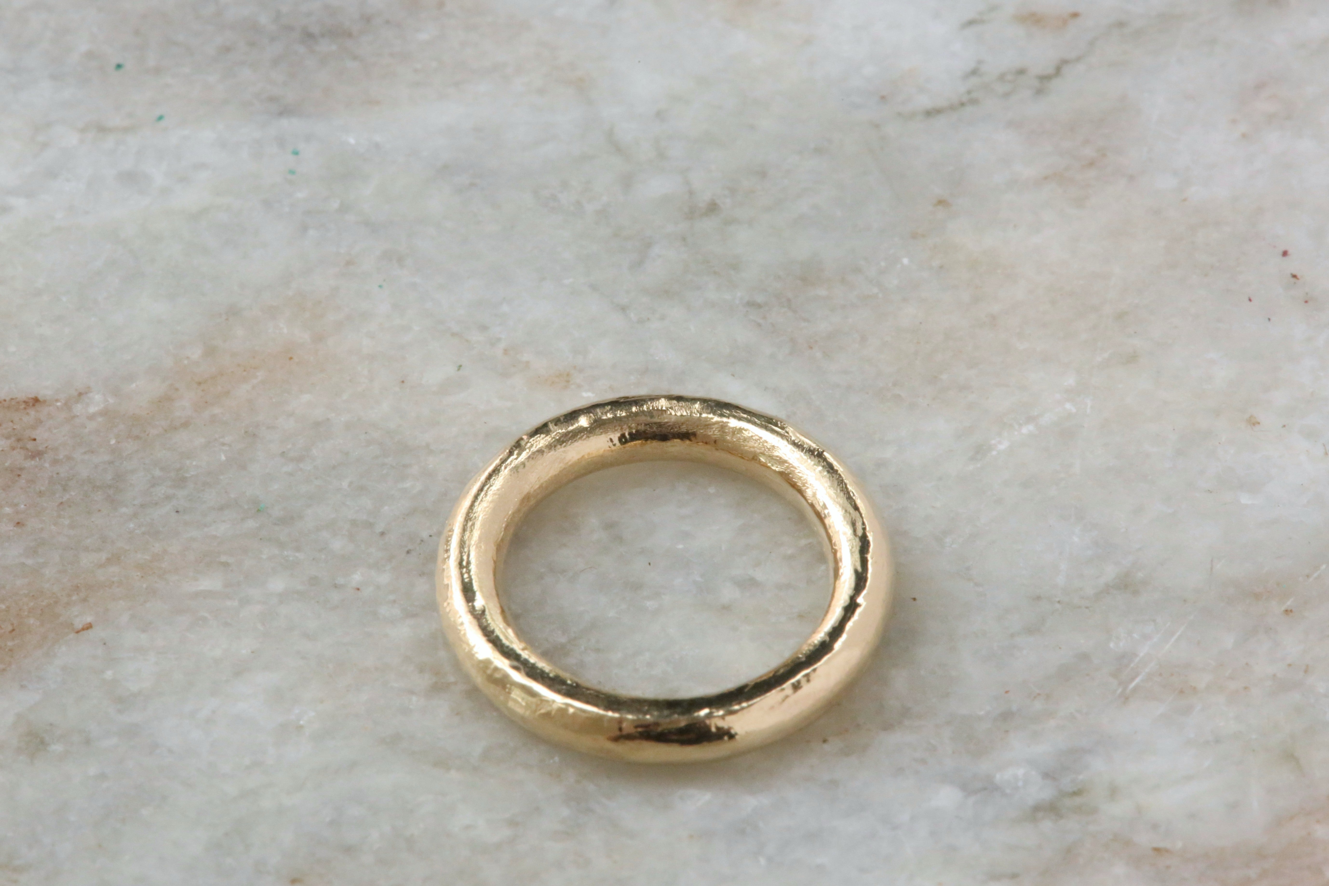 A textured gold band ring resting on a light beige marble surface.
