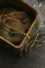 A gold snake chain necklace draped inside an ornate vintage bronze jewelry box on a dark textured surface.