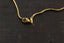 A close-up of a gold snake chain necklace with a lobster clasp and toggle closure, laid on a dark textured surface.
