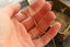 A close-up of a hand holding a thin gold chain necklace against a softly blurred background with a decorative box.