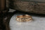 The Gate band is an intricately hand-carved wedding band of woven leaves and arch ways, wrought into reclaimed golds, designed by The North Way Studio. Shown here in a closeup atop a white marble tabletop.