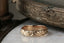 The Gate band is an intricately hand-carved wedding band of woven leaves and arch ways, wrought into reclaimed golds, designed by The North Way Studio. Shown here atop a white marble tabletop.